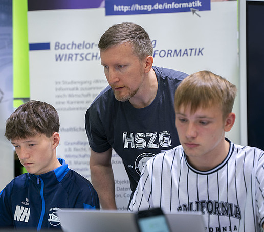HSZG employee informs two seated students at the laptop.